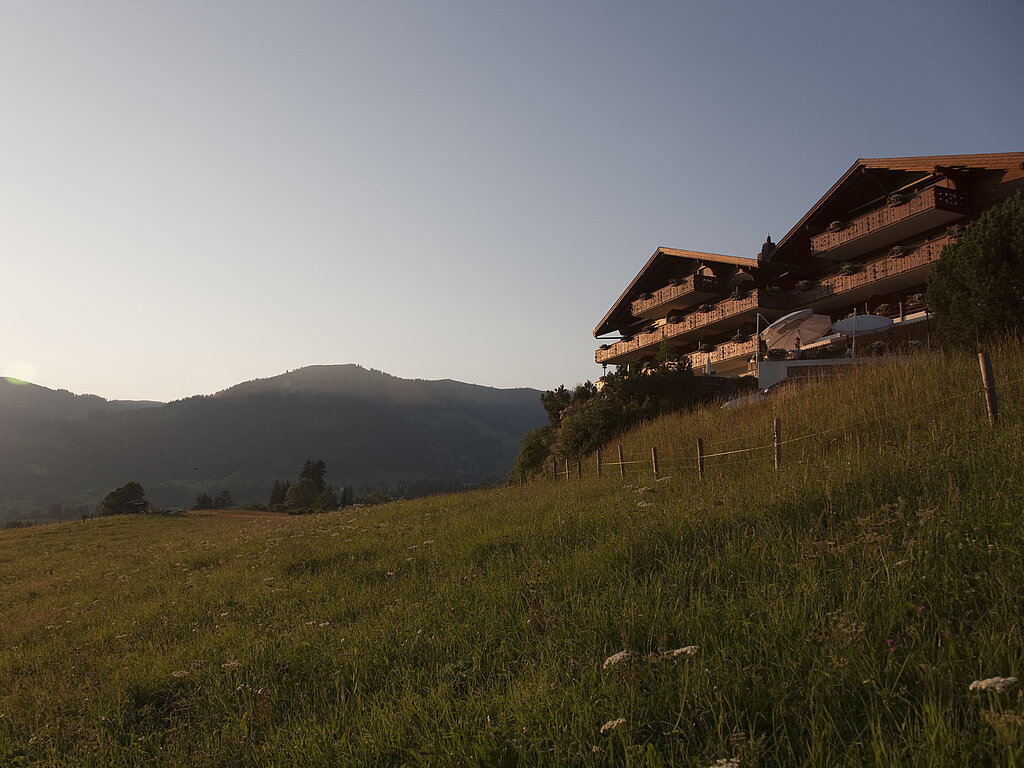 <p>Das Hotel Le Grand Chalet auf einem Hügel, blauer Himmel, ein Feld mit Bäumen und ein Berg im Hintergrund.</p>