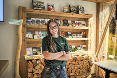 Mitarbeitende von Gstaad Saanenland Tourismus steht vor einem Holzregal mit Prospekten und Informationsmaterial im Tourismusbüro Gstaad.