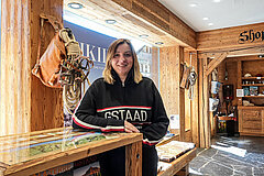 Person at the reception desk of the Gstaad Tourist Office in a rustic interior with information materials, wooden furnishings and souvenir items.