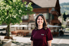 Personne debout à l’extérieur devant un bâtiment en bois traditionnel dans un village alpin, portant un t‑shirt avec le logo Gstaad.