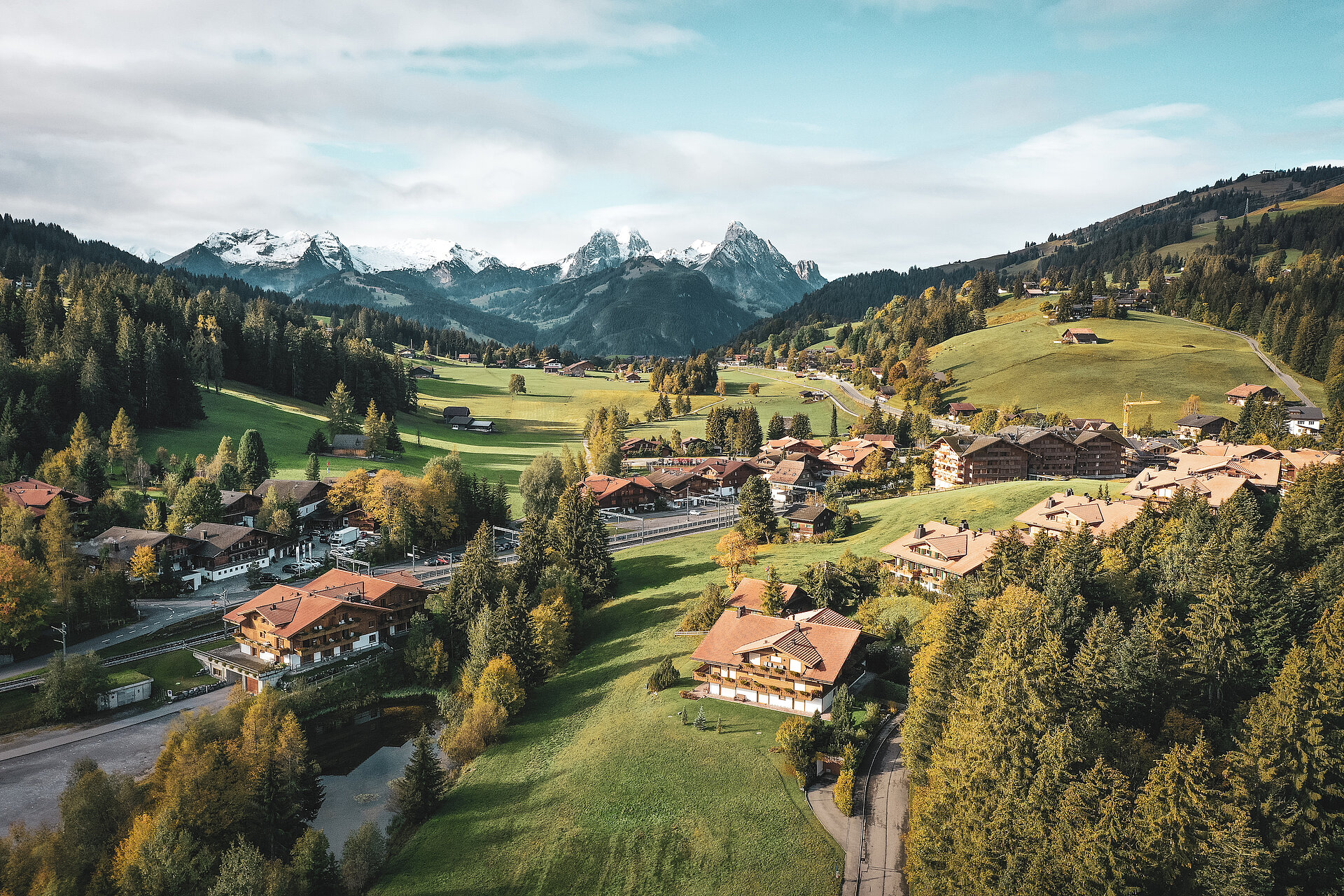 Aus der Vogelperspektive sieht man das Dorf Saanenmöser im Sommer. Die Flächen rund ums Dorf sind grün und im Hintergrund sieht man höhere Berge.