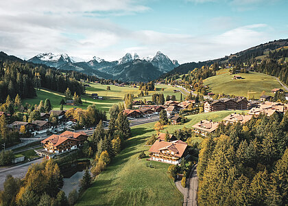 Aus der Vogelperspektive sieht man das Dorf Saanenmöser im Sommer. Die Flächen rund ums Dorf sind grün und im Hintergrund sieht man höhere Berge.