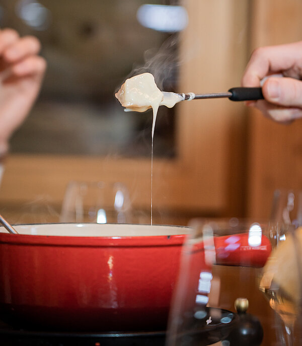 Rotes Fondue Caquelon mit ziehendem Käse und drei Händen mit Fondue-Gabeln.