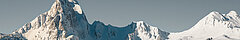 Joli paysage de montagnes enneigé, constitué de parois rocheuses, de pistes enneigées, de forêts et de chalets.