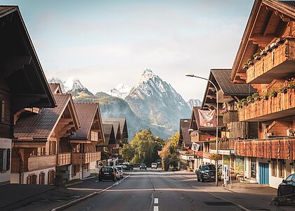 Eine malerische Dorfstraße mit traditionellen Chalets und Blick auf majestätische Berge im Hintergrund. Die Umgebung ist ruhig und idyllisch, ideal für einen entspannenden Aufenthalt.
