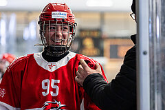 Ice hockey player wearing a red jersey with number 95 and a helmet at the team bench indoors.