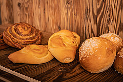 Auf einem braunen Holzgestell liegen verschiedenen Patisserie. Links steht eine Nuss-Schnecke, gefolgt von zwei Vanille-Gipfeln und drei Berliner mit Zuckerguss.