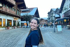 Person mit langen Haaren auf der Promenade von Gstaad. Im Hintergrund sind traditionelle Chaletgebäude, Geschäfte und die charakteristische Dorfatmosphäre zu sehen.