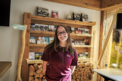 Mitarbeitende von Gstaad Saanenland Tourismus vor einem rustikalen Holzregal mit Broschüren, Karten und Informationsmaterial im Tourismusbüro Gstaad.