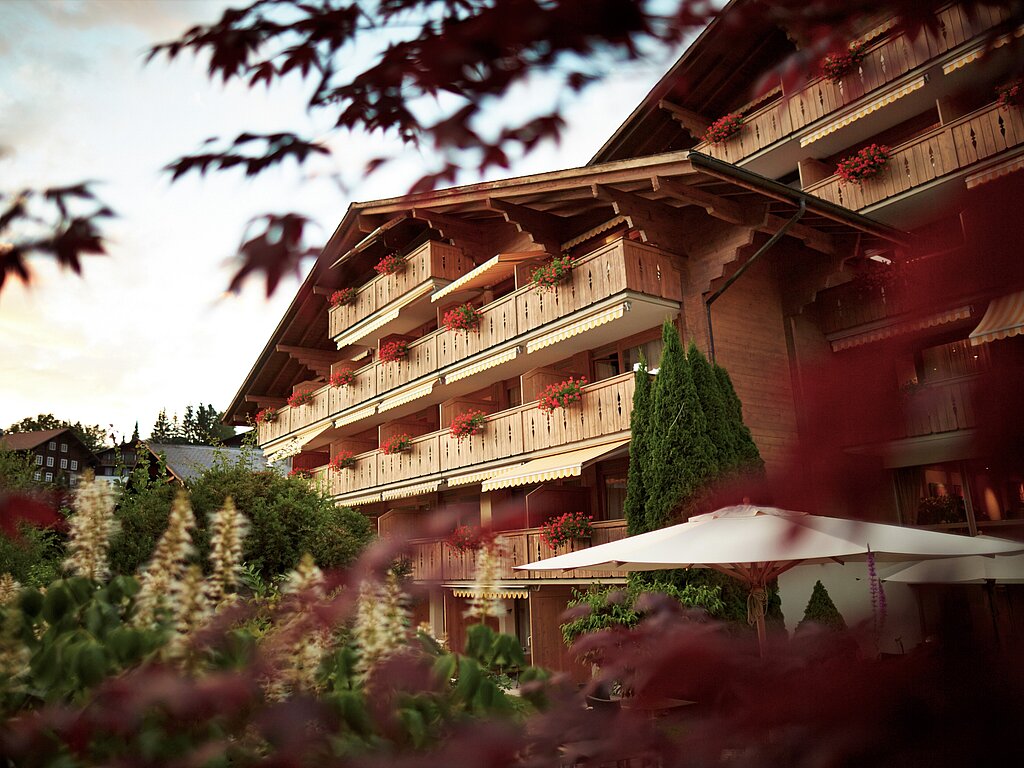 <p>Das Hotel Gstaaderhof mit Balkonen und Blumen. Im Vordergrund steht eine Gruppe von Bäumen.</p>