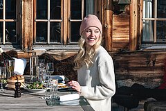 Person seated at a set table on a sunny outdoor restaurant terrace in front of a traditional wooden building.