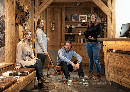 In einem urchigen Empfangsbüro erwarten drei Frauen und ein Mann gespannt ihre Gäste.