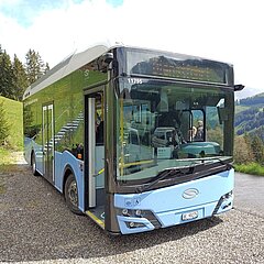 Blaues Elektro-Postauto fährt auf einer schönen Bergstrasse in Abländschen.