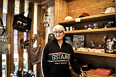 Person inside a souvenir shop with wooden walls, shelves and clothing featuring Gstaad branding.