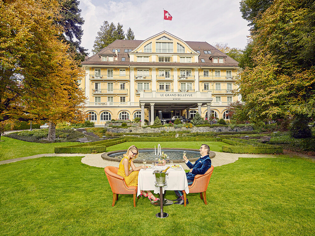 <p>Auf dem grünen Rasen vor dem Hotel Le Grand Bellevue sitzen ein Mann und eine Frau an einem Tisch.</p>