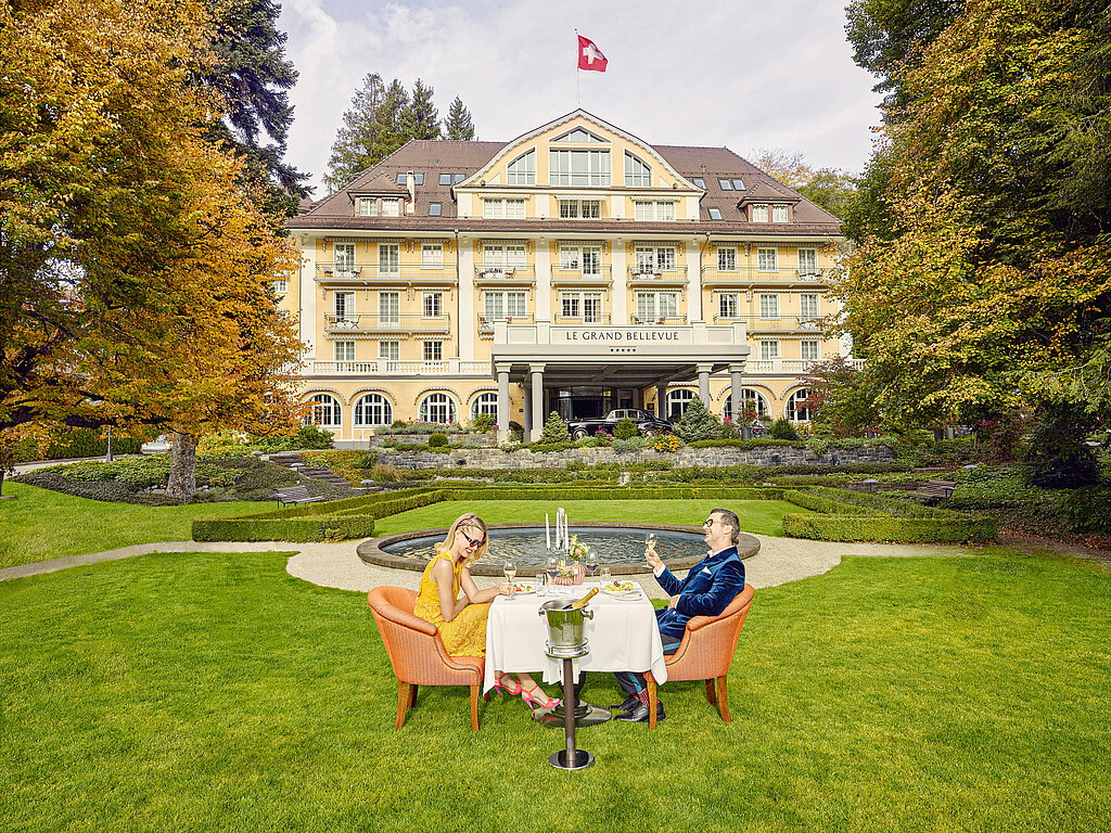 Auf dem grünen Rasen vor dem Hotel Le Grand Bellevue sitzen ein Mann und eine Frau an einem Tisch.