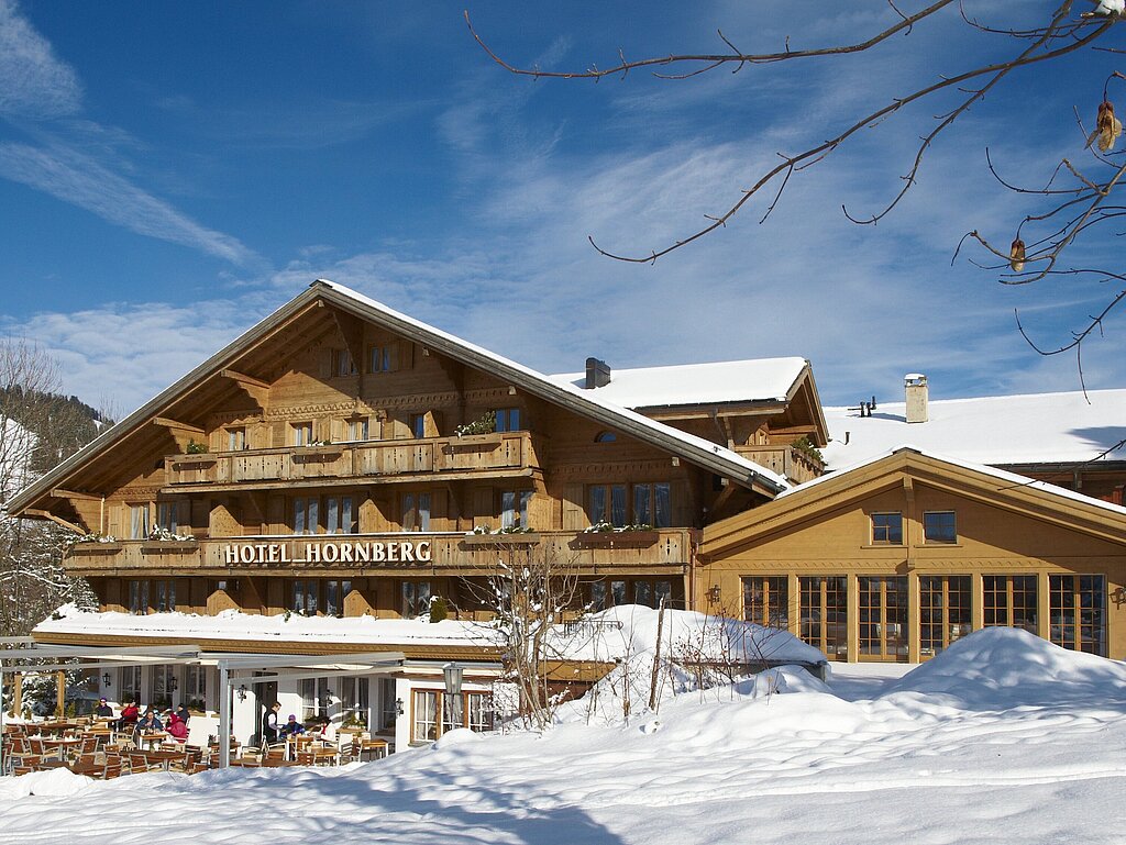 Hölzernes Hotel Hornberg bei Sonnenschein und Schneebedeckter Piste.