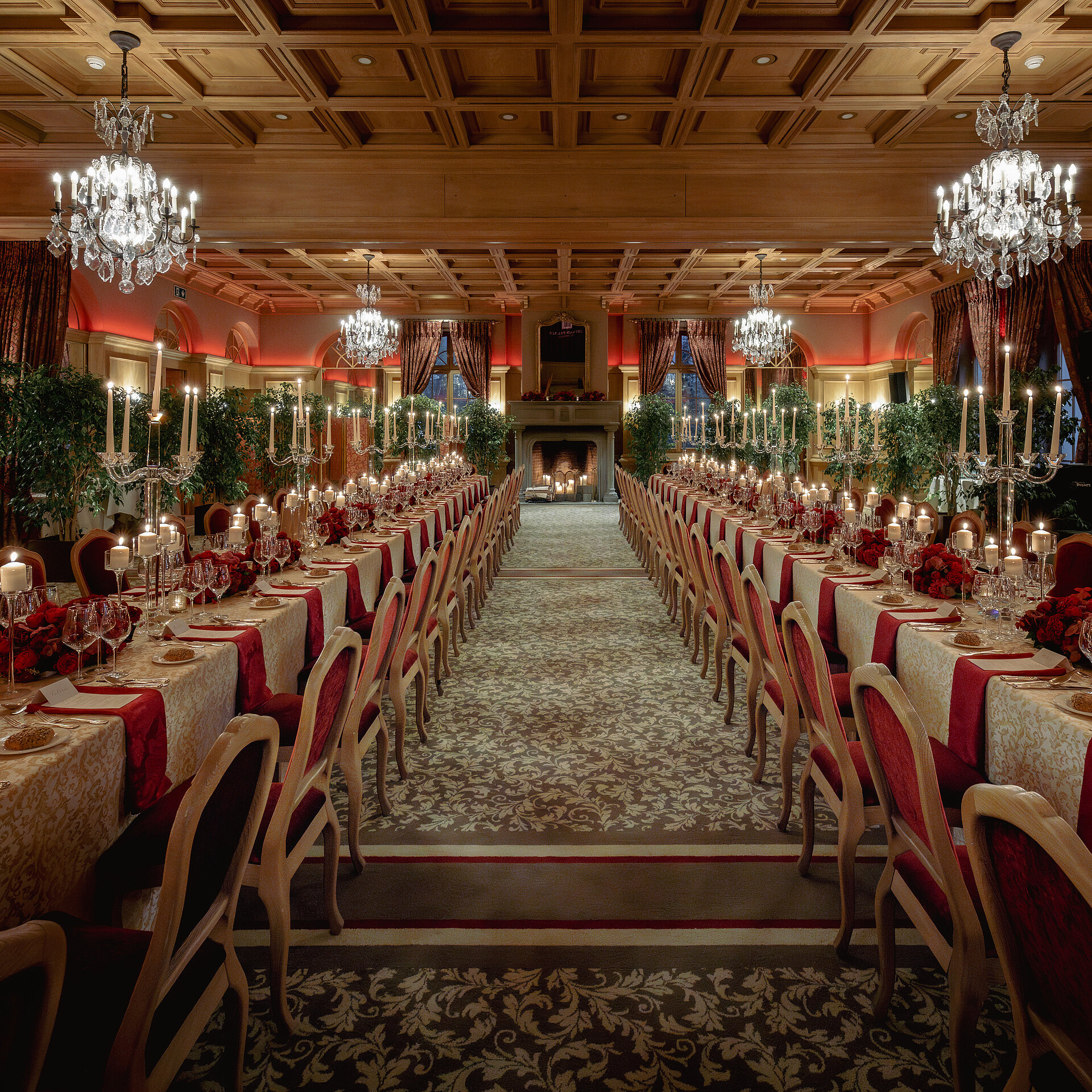In einem luxuriösen Saal steht ein langer Tisch mit Kerzen, Weingläsern und Blumen.