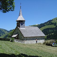 Vor einer kleinen Kirche gabelt ein Bauer getrocknetes Gras auf sein Gefährt